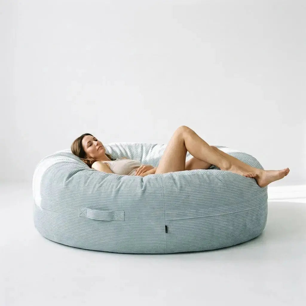 A woman relaxes on a Saccosäck Roll 190 Waves Mint bean bag in a minimalist, light-filled room.