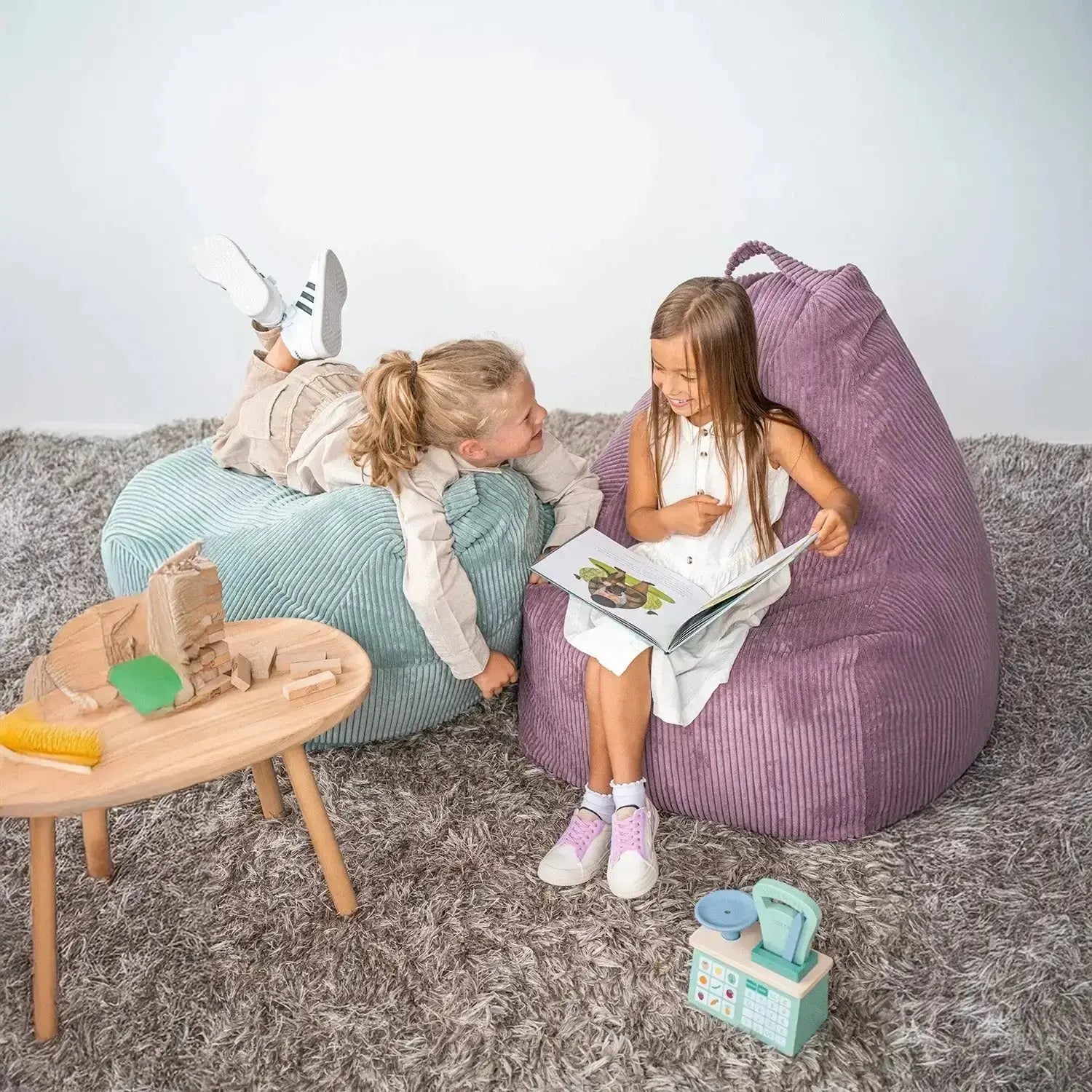 Barnmöbler för barn och ungdomar: två barn sitter på sittsäckar och läser en bok tillsammans.