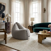 Modern living room with a grey beanbag chair, green velvet sofa, brass coffee table, and minimalist decor.