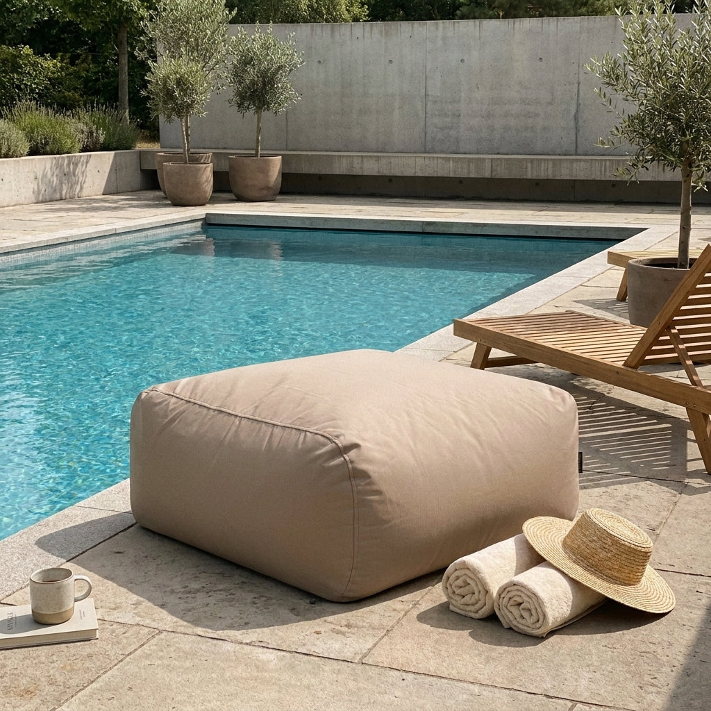 Sittsäck Tube Sittpuff 80 Colorin Taupe displayed poolside on a stone patio with towels and a sun hat.