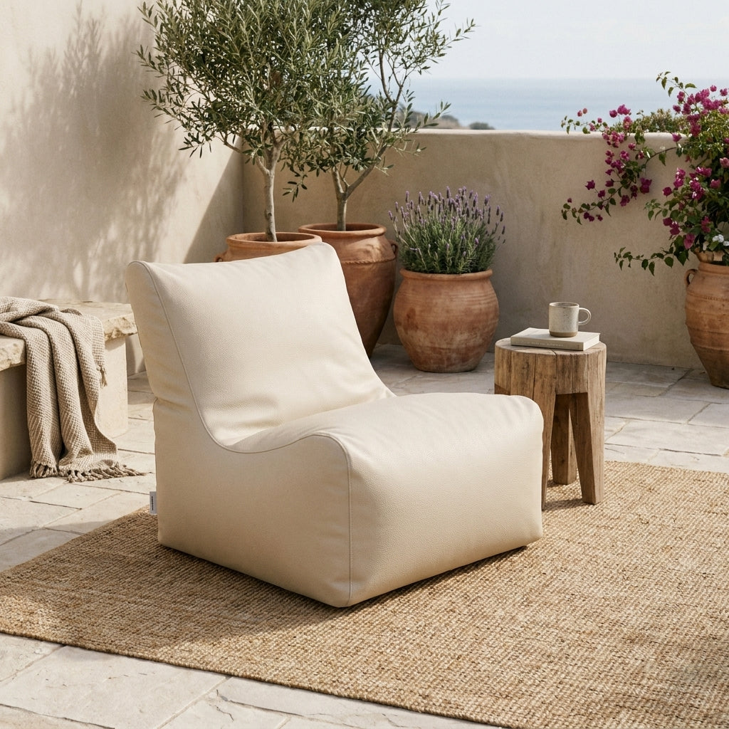 Sittsäck Fåtölj Seat 100 Outside Beige styled on a patio with a rug, wooden side table, and Mediterranean plants.