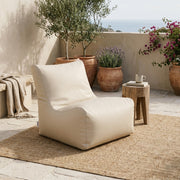Sittsäck Fåtölj Seat 100 Outside Beige styled on a patio with a rug, wooden side table, and Mediterranean plants.