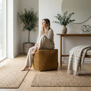 A woman sits on a mustard corduroy Sittpuff Up! Waves ottoman in a cozy, minimalist living room with natural decor.