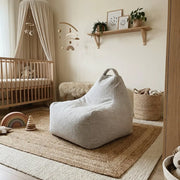 Boho-style nursery featuring a cozy teddy beanbag chair, wooden crib, neutral decor, and a layered jute rug.