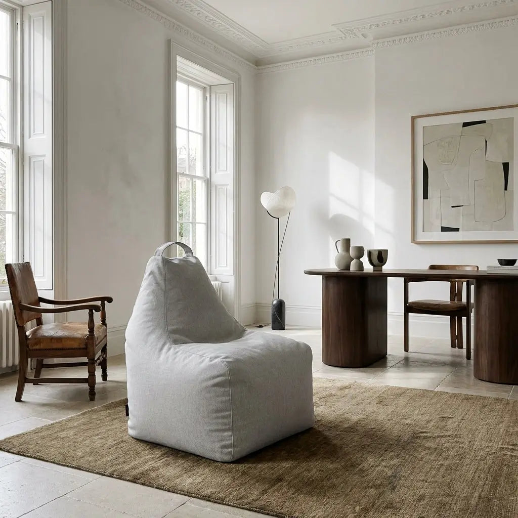 Modern minimalist living room featuring a grey beanbag chair, wooden dining table, and abstract art in a bright, airy space.