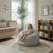 Cozy, modern neutral nursery featuring a child on a corduroy bean bag chair, wooden crib, and minimalist decor.
