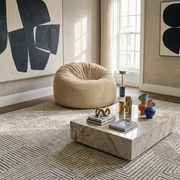 Modern living room with a beige beanbag chair, marble coffee table, abstract wall art, and geometric patterned rug.