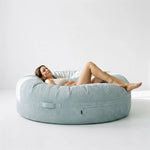 A woman relaxes on a Saccosäck Roll 190 Waves Mint bean bag in a minimalist, light-filled room.