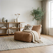 Modern minimalist living room featuring a beige lounge chair, textured throw blanket, and stacked books on a chunky rug.
